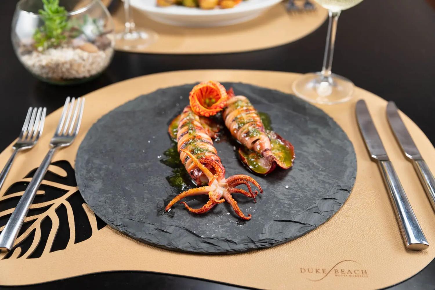 Lulas servidas com molho sobre uma base escura, em mesa posta do restaurante.