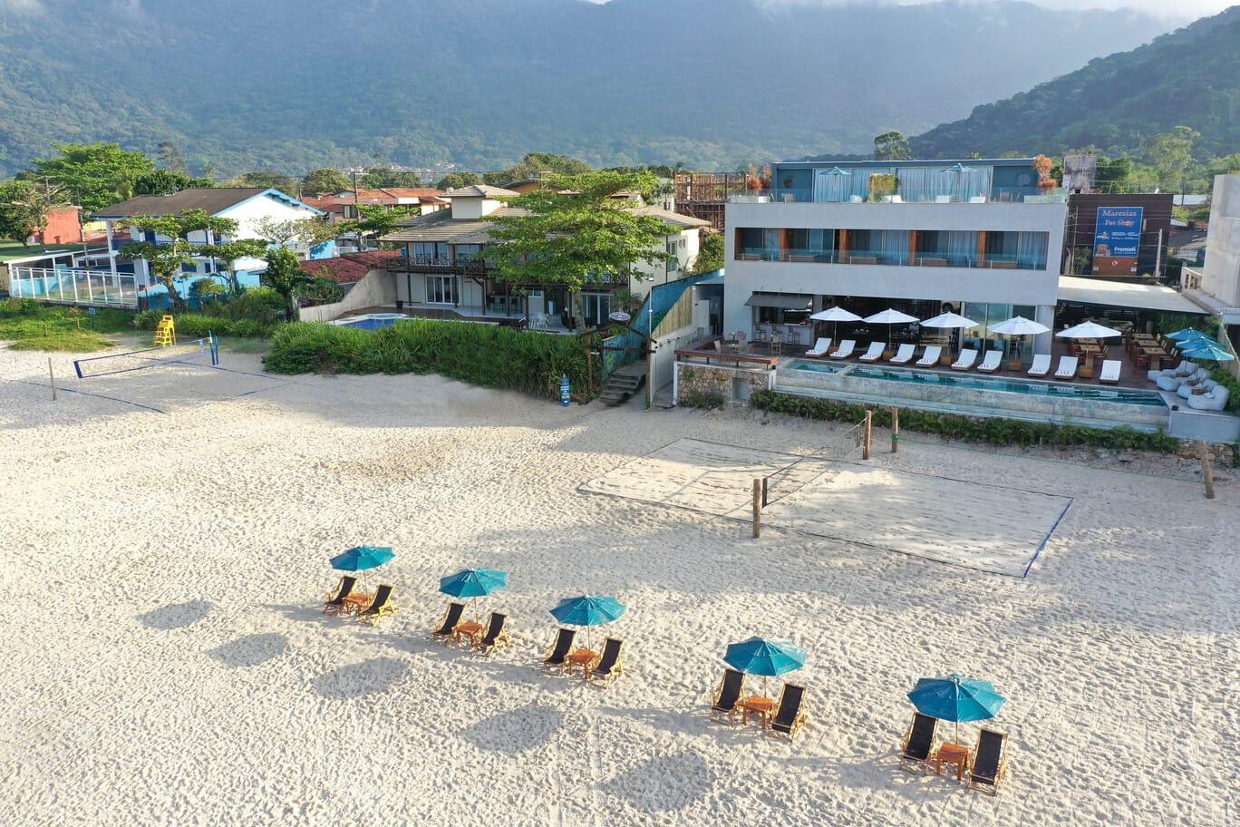Edifício Praia diante da areia, com espreguiçadeiras e guarda-sóis turquesa.