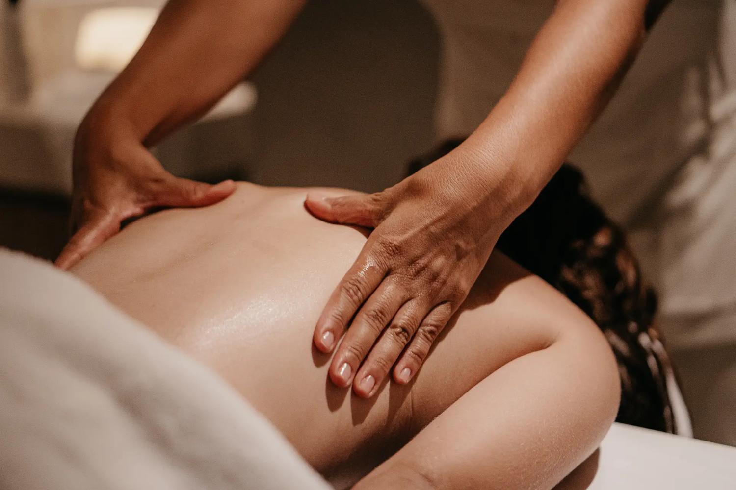 Mãos realizando uma massagem nas costas durante um atendimento no SPA.